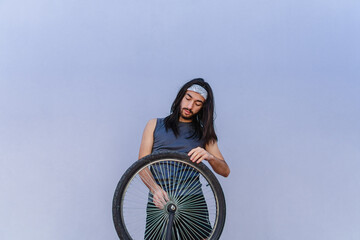Young Hispanic Latin man with long hair, wearing sportswear, fixing his bicycle tire, copy space
