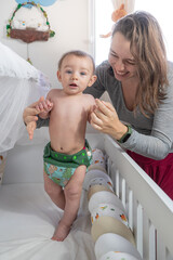 Mãe brincando com bebê no berço rindo com fralda ecológica. Conceito Eco