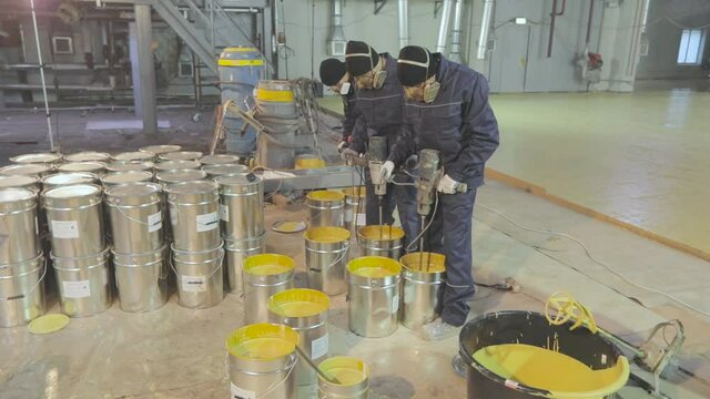 Shiny barrels with self-leveling floor workers in the background. Paint cans at a construction site. Metal drums at a construction site