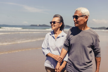 Romantic Senior couple strolling happily along the beach in the sunshine and bright sky. Plan life...