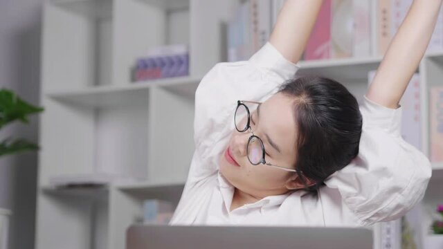 Asian young woman working on laptop and taking a rest, raising her hands up, doing some stretching and back to work. Having own business. Working at home concept
