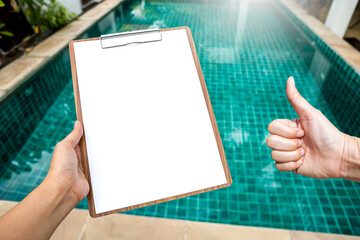 Good water quality, Girl hand holding blank paper clipboard over clear swimming pool water...