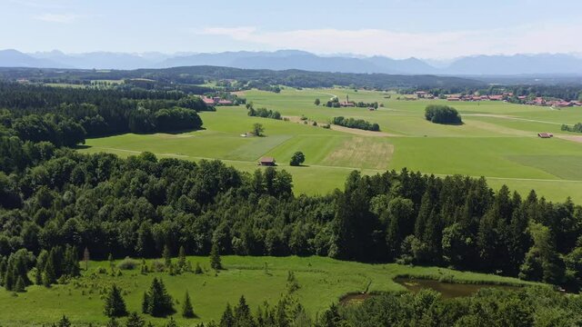 Idyllic bavarian summer landscape, filmed from above, panning right, in mountain range of the alps with a little pond and green meadows in the foreground