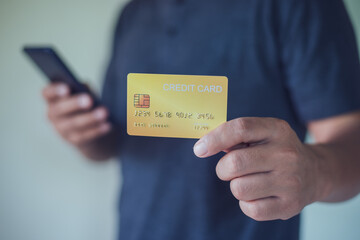 Man holding a credit card and using smart phone for online payment, using online banking application on his cell phone.