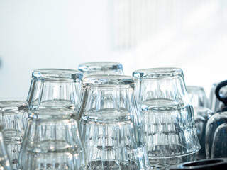 Close up upside down empty drinking water glasses. Stacks of clean and dried empty glass on white wall background in cafe.