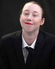 Young woman with short blonde hair poses before a dark background.