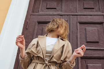 Young millennial woman with wild hair dressed in an autumn coat posing near the door of an old building.