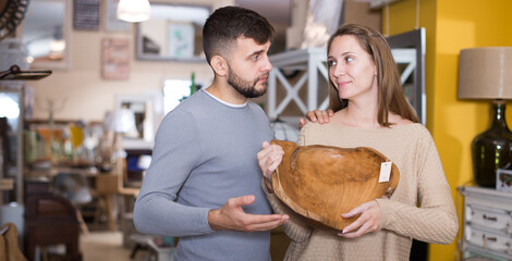 Portrait of loving couple with stylish wooden dish in shop of secondhand furniture