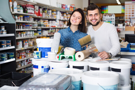 Young Smiling Couple Demonstrating Tools For House Renovating In Paint Supplies Store