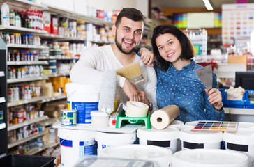 Glad active young couple buying tools for house decoration in paint supplies store