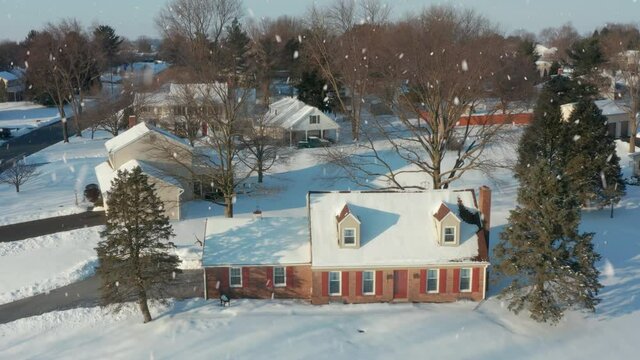 Brick Cape Cod home in winter snow. Peaceful house in cold American Christmas scene. USA neighborhood establishing aerial shot.