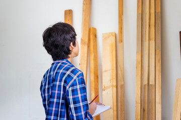 Young carpenter checking woodwork stock at factory storage. Man counting timber beams wood inventory in carpentry workshop