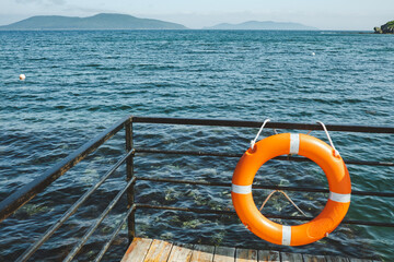 bright orange lifebuoy on pier, clear blue beautiful sea around. safety on water. selective focus