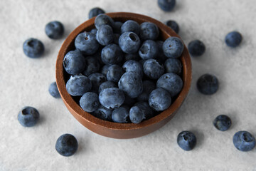 Closeup heap of super food fresh blueberries rich in vitamin c and antioxidants in dark brown wooden bowl on white grey stone background. Healthy eating and lifestyle concept