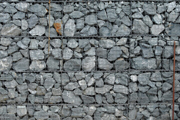 The texture of a fence made of many gray stones, reinforced with a metal mesh.