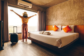 Portrait of tourist woman raised her hands while standing nearly window, looking to view outside...