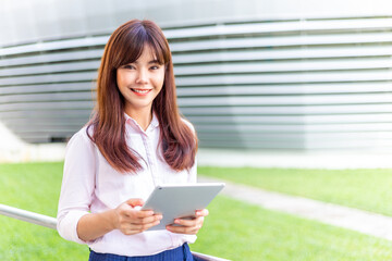 Fototapeta premium Happy young attractive business woman in her pink shirt using her tablet computer to check her social media outside of her office building