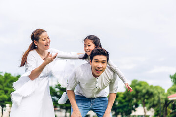 Portrait of enjoy happy love asian family father and mother holding little asian girl on back smiling playing and having fun moments good time in summer park at home