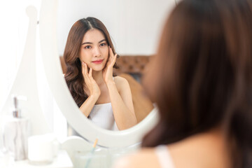 Obraz na płótnie Canvas Smiling of young beautiful pretty asian woman clean fresh healthy white skin looking at mirror.asian girl touching on her face with hand and applying cream at home.spa and beauty concept