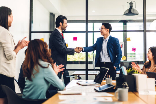 Image two asian business partners in elegant suit successful handshake together in front of group of casual business clapping hands in modern office.Partnership approval and thanks gesture concept