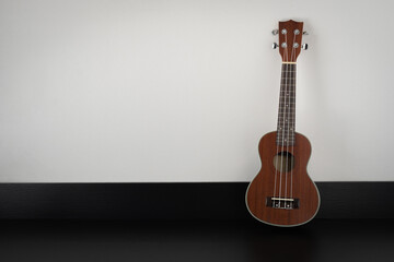 A ukulele guitar is placed on a black patterned table on the right, white background, with copy space. Music creates joy and luxury in the summer holiday background. Travel and lifestyle ideas.