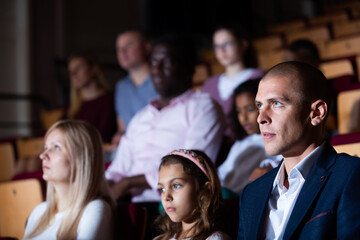 Portrait of adult man sitting in theater hall, absorbed in watching stage performance