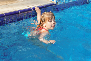 little girl swims in a swimming pool with blue water on a summer day