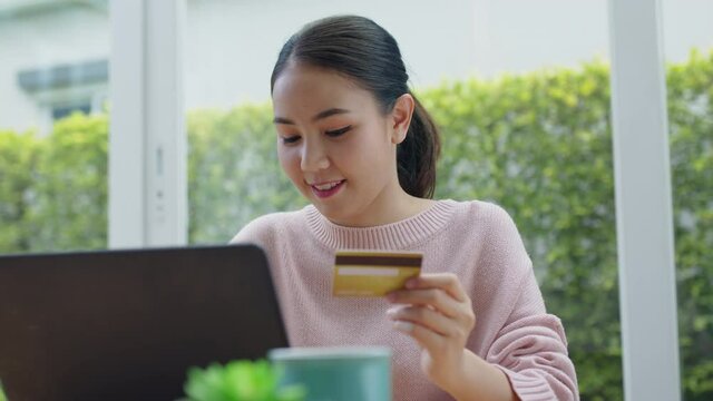 Young asia people sit relax smile enjoy gift card typing secure code data in social media e-commerce retail shop in notebook at comfort home on desk table. Remotely buy at store via omnichannel tech.