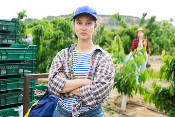 Portrait of a focused confident farmer woman standing in a fruit nursery at the gathering of ripe cherries. ..Close-up portrait