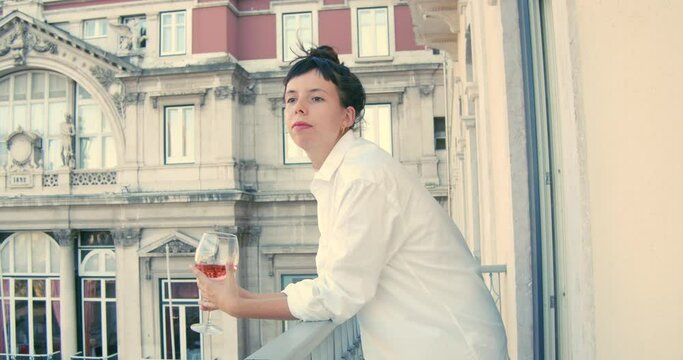 Cute woman drinking a glass of rose wine in a balcony wearing only a shirt. European lifestyle.