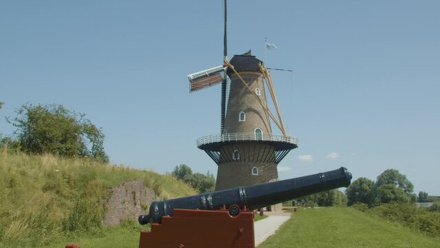 Wide shot of traditional windmill spinning with a black cannon in the foreground