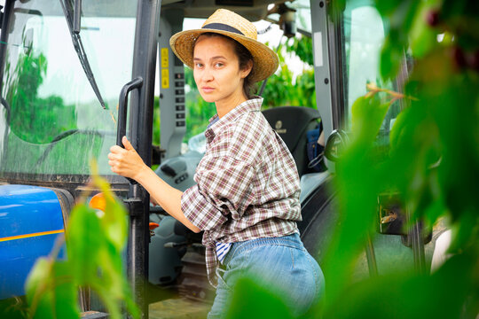 Hardworking Female Farmer Working In A Fruit Nursery Climbs Into The Cab Of A Tractor To Get Behind The Wheel