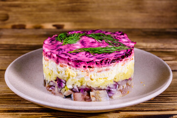 Ceramic plate with russian traditional new year salad herring under fur coat (shuba) and on rustic wooden table