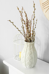 Vase with willow branches on shelf near light wall