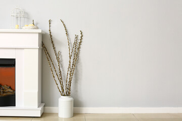 Vase with willow branches and modern fireplace near light wall
