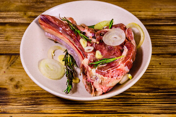 Raw ribeye steak, spices, rosemary, onion and garlic in a ceramic plate on wooden table