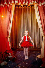 Small girl during a stylized theatrical circus photo shoot in a beautiful red location. Young model...