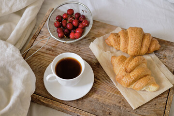 Tasty breakfast with fresh croissant, coffee, cherries on a wooden tray. Espresso on a breakfast tray