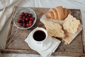 Tasty breakfast with fresh croissant, coffee, cherries on a wooden tray. Hearty croissant with tomato and cheese. Espresso on a breakfast tray