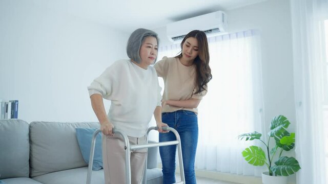 Asian young daughter support senior disabled woman walking with walker