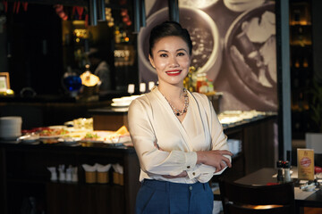 Portrait of happy smiling elegant middle-aged woman standing at bar counter of restaurant she is opening