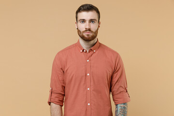 Beautiful ecstatic fun tatooed young brunet man 20s short haircut with earrings wear apricot shirt look camera isolated on pastel orange background studio portrait. People emotions lifestyle concept,