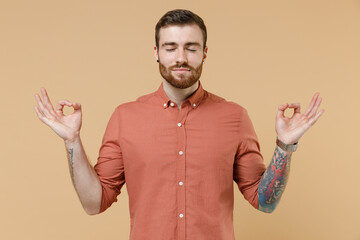 Spiritual tranquil tatooed young brunet man 20s short haircut with earrings wears apricot shirt...