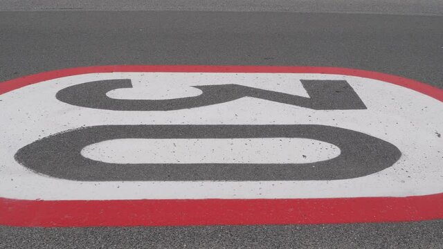Car passing a 30 km h horizontal speed limit sign painted on an asphalt road.