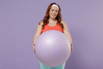Fototapeta premium Young fun smiling happy chubby overweight plus size big fat fit woman 20s wearing red top warm up train holding fit ball isolated on purple color background gym home. Workout motivation sport concept.