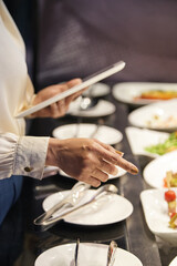 Hands of restaurant manager with digital tablet checking readiness of appetizers and salads for guests