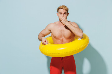 Handsome young sexy lifeguard man 20s in red shorts swimsuit relax near hotel pool hold inflatable...