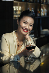 Portrait of happy elegant woman with glass of red wine sitting at bar counter in restaurant