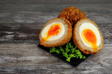 Two Scotch eggs one cut in half showing orange yolk and pork sausage meat