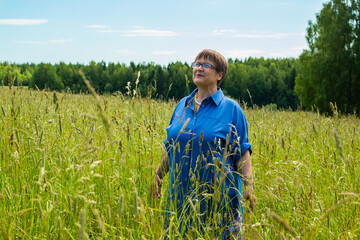 Naklejka na ściany i meble Grandma is standing in the field. An elderly woman is resting in nature.
